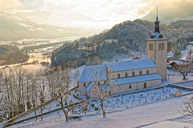 Invierno en Suiza. Pintoresco paisaje montañoso cubierto de nieve cerca del castillo de Gruyeres con una antigua iglesia en primer plano.