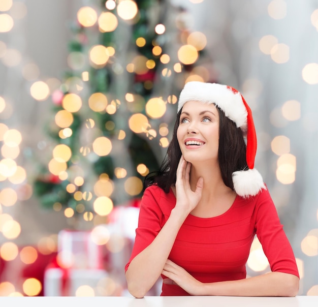 invierno, vacaciones, felicidad y concepto de la gente - mujer sonriente con sombrero de ayudante de santa sobre fondo de luces de árbol de Navidad