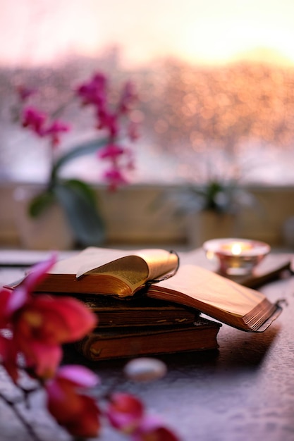 Invierno con velas en la pila de libros antiguos Puesta de sol ventana naranja brillo rosa y orquídea fucsia