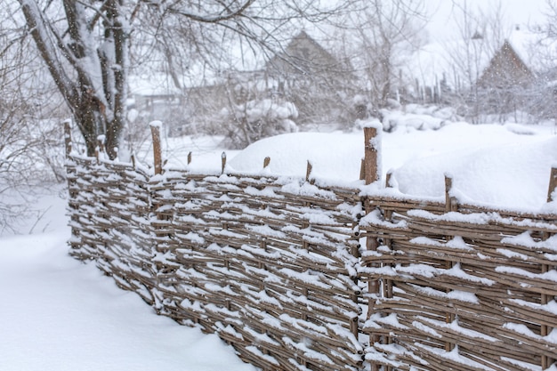 Invierno viejo valla de mimbre tambaleante hecha de tablas de madera. Tormenta de nieve