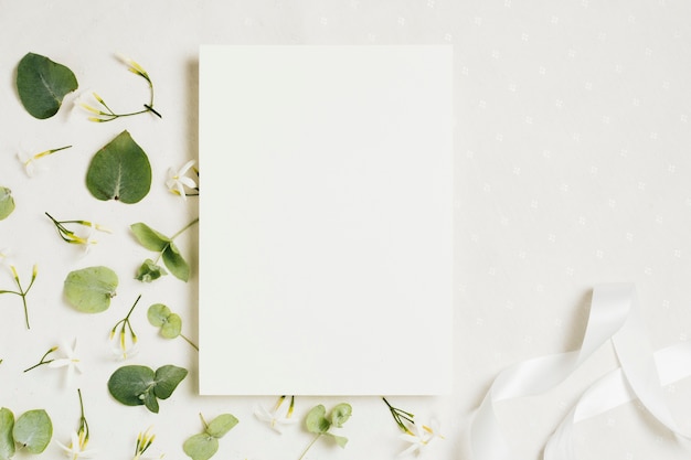 Invitación de boda en blanco blanco con flores y cinta de jasminum auriculatum sobre fondo blanco