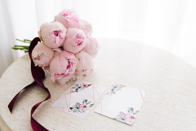 Invitaciones de boda junto a un hermoso ramo de peonías rosas