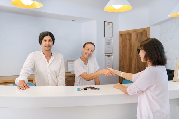 Invitado en el hotel, recepcionistas hombres y mujeres saludando a mujer