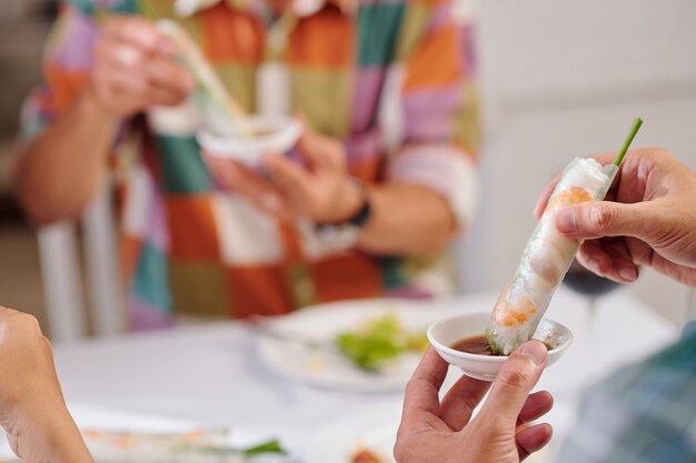 Los invitados a la cena festiva comiendo rollitos de primavera tradicionales con salsa picante en la cena, enfoque selectivo