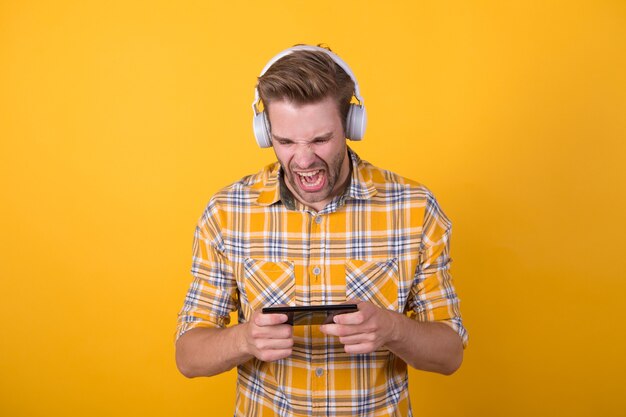 Involucrado en juegos. Obtenga una suscripción de música. Hombre satisfecho escuchar música con auriculares modernos y smartphone. Las mejores aplicaciones de música que merecen ser escuchadas. Guy aplicación móvil de usuario moderno. Concepto de música fresca.
