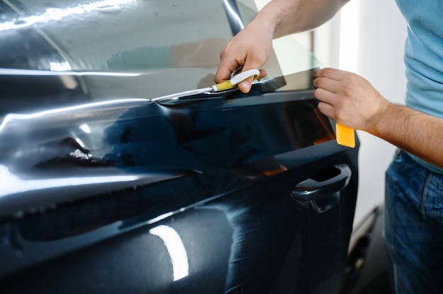 Invólucro masculino contém filme protetor solar, serviço de tingimento de carro. trabalhador aplicando tinta de vinil na janela do veículo na garagem