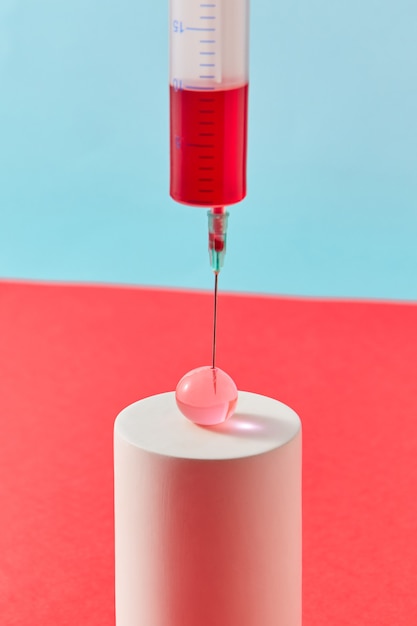 Inyección de composición medicinal de jeringa de plástico desechable con líquido rojo en una pequeña bola transparente