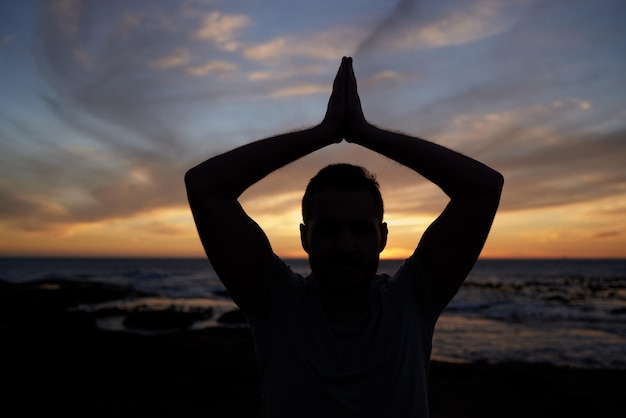 Ioga ao pôr do sol e fitness na praia com um homem flexível malhando para exercícios e força Silhueta do oceano e iogue masculino se esforçando para iluminação espiritual e de chakra enquanto medita ao ar livre