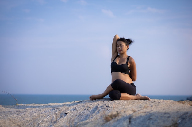 Ioga asiática da mulher gravida nas horas de verão do sol da praia