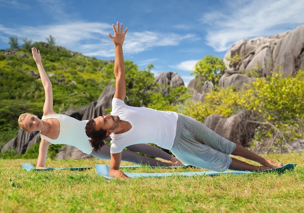 ioga, fitness, esporte e conceito de pessoas - casal fazendo exercícios de prancha em esteiras ao ar livre