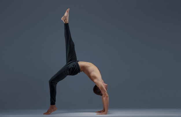 Ioga masculina, fazendo exercícios de alongamento em fundo cinza. Homem forte praticando ioga, treinamento de asana, concentração máxima, estilo de vida saudável