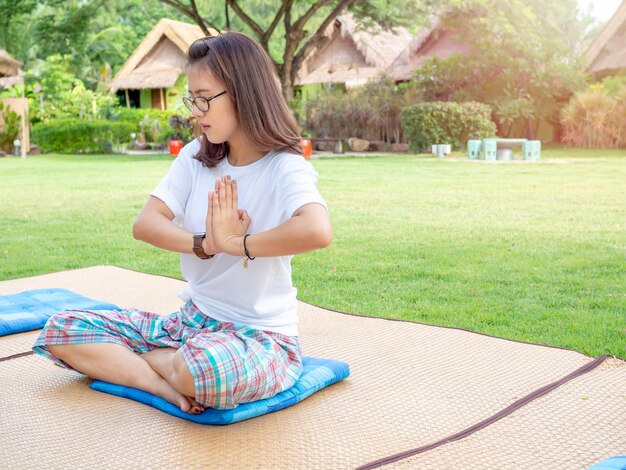 Ioga no parque Mulher asiática usando óculos fazendo exercícios de ioga ao ar livre na almofada no tapete no gramado