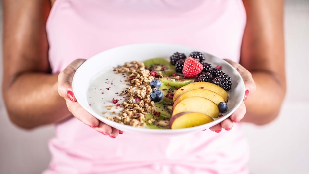 Iogurte amora muesli framboesas mirtilos kiwi e pêssegos em uma tigela segurando jovem