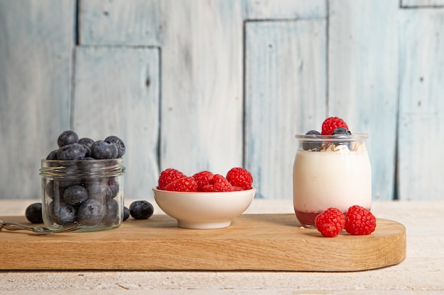 Iogurte branco com framboesas frescas, mirtilos e muesli em uma placa de servir na mesa rústica na mesa de madeira