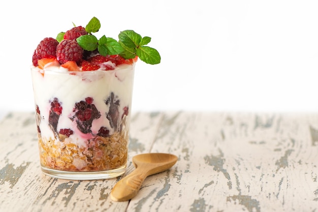 Iogurte com cereais e frutas em vidro na mesa de madeira clara.