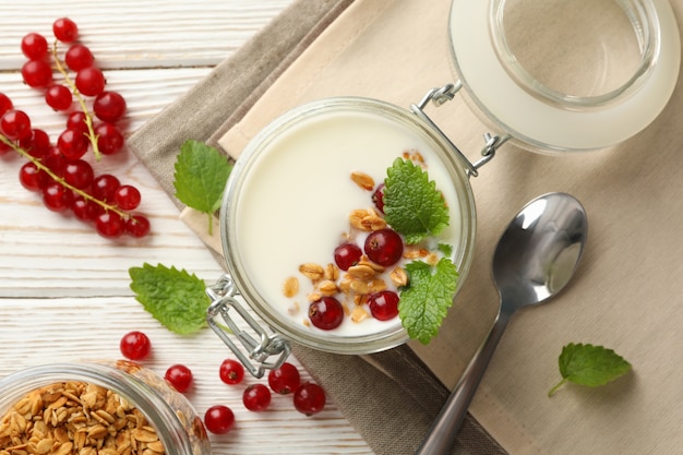 Iogurte com cranberry, granola e hortelã em fundo branco de madeira