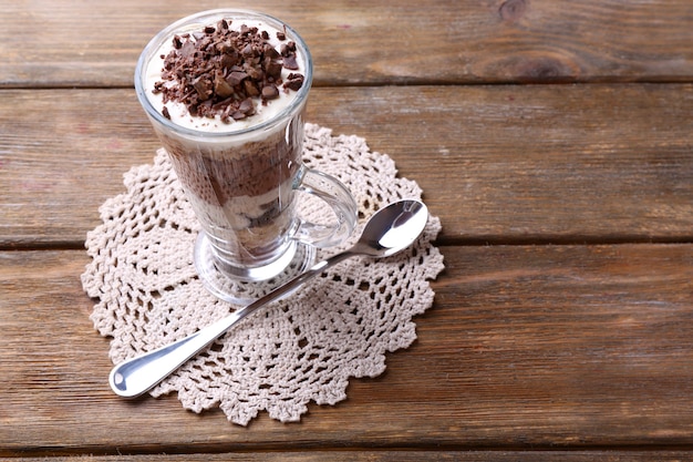 Iogurte, com creme de chocolate, chocolate picado e muesli servido em taça em espaço de madeira