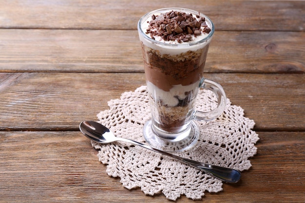 Foto iogurte com creme de chocolate picado chocolate e muesli servido em vidro com fundo de madeira