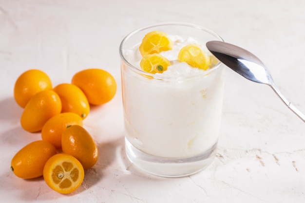 Iogurte com fatias de kumquat em copo com colher de metal e frutas inteiras