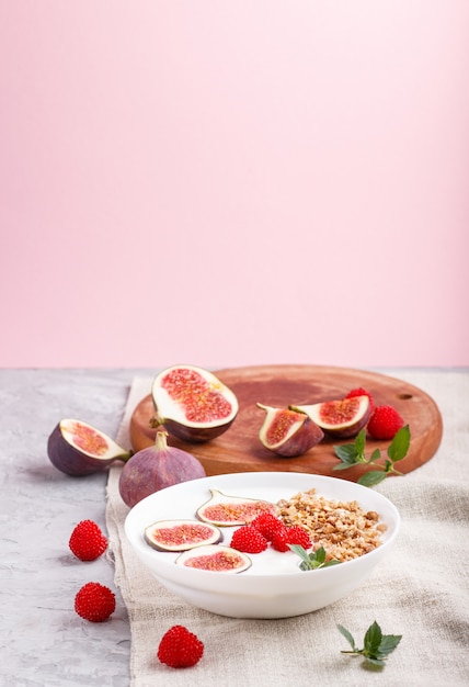 Iogurte com framboesa, granola e figos em chapa branca sobre um fundo cinza e rosa