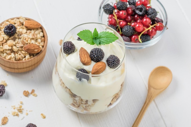 Iogurte com granola amoras e amêndoas em um copo de vidro em uma mesa branca