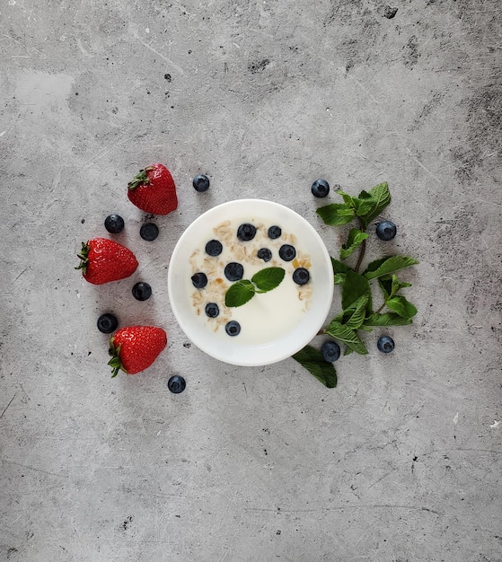 Iogurte com mirtilos frescos e muesli em um prato branco, morangos e em um fundo leve