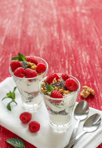 Iogurte com sementes de chia, nozes, hortelã e framboesas na mesa vermelha fechar com espaço de cópia