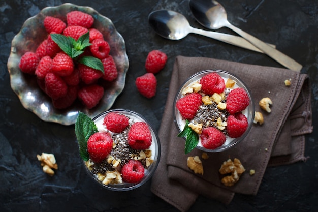 Iogurte com sementes de chia, nozes, hortelã e framboesas no escuro de perto