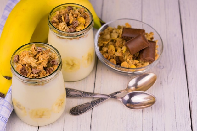 Iogurte de banana com granola ha branco fundo de madeira.