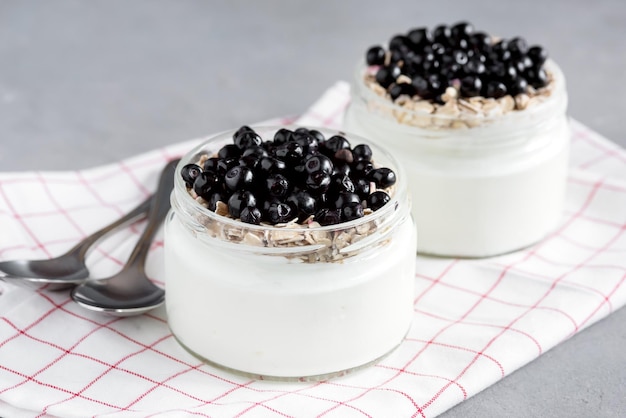 Iogurte de café da manhã saudável com mirtilos e muesli servido em frasco de vidro na cor de fundo de madeira