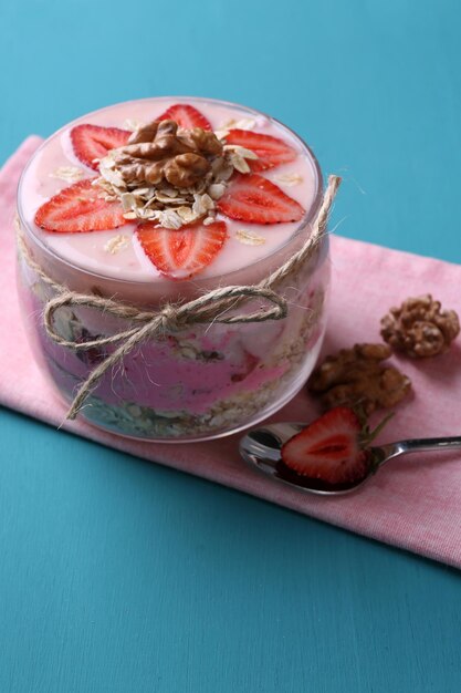 Iogurte de café da manhã saudável com morangos e muesli servido em frasco de vidro na cor de fundo de madeira