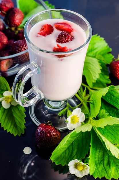 Iogurte de morango e frutas e flores de morango na mesa preta