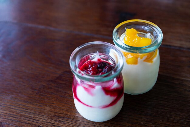 Iogurte grego com frutas e manga em potes de vidro com fundo de madeira