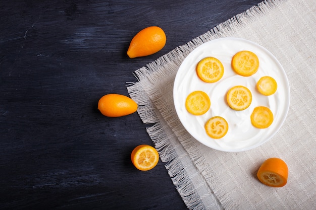 Iogurte grego com pedaços de kumquat em um prato branco sobre um fundo preto de madeira