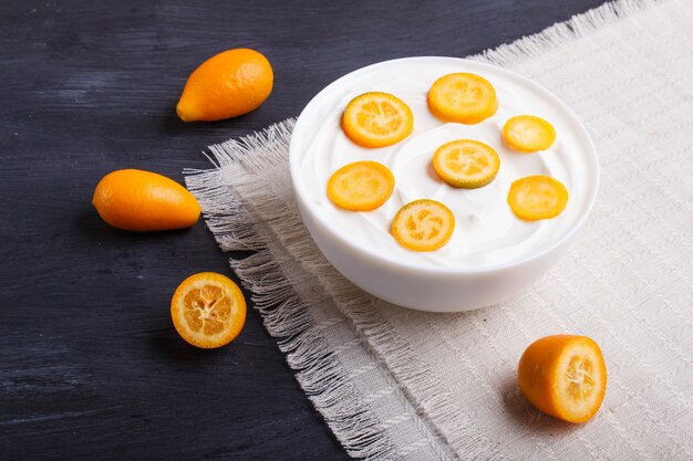 Iogurte grego com pedaços de kumquat em um prato branco sobre uma mesa de madeira preta