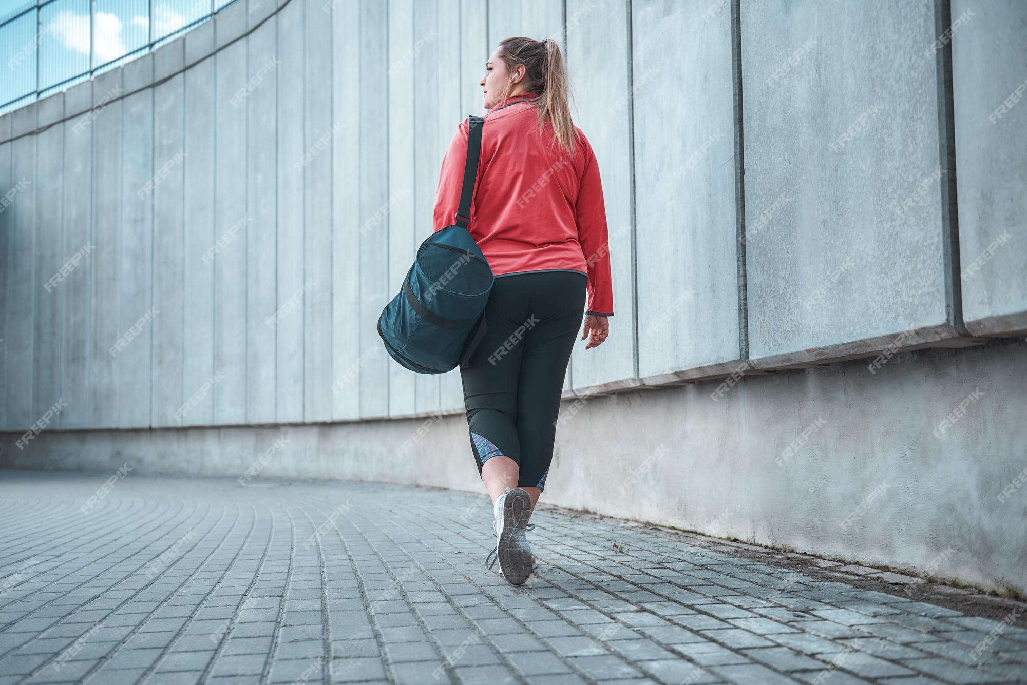 Ir a casa. vista posterior la mujer de talla grande en ropa deportiva llevando su bolso y yendo a casa después de hacer ejercicio al concepto de deporte. mujeres