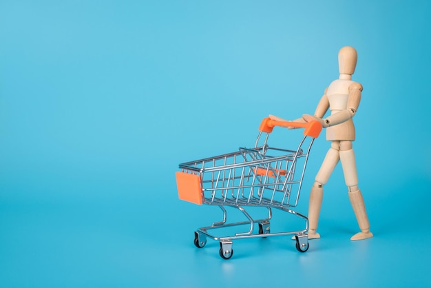 Ir de compras concepto. Foto de una figura masculina de madera que lleva una tarjeta de carrito vacía aislado fondo azul con espacio para texto