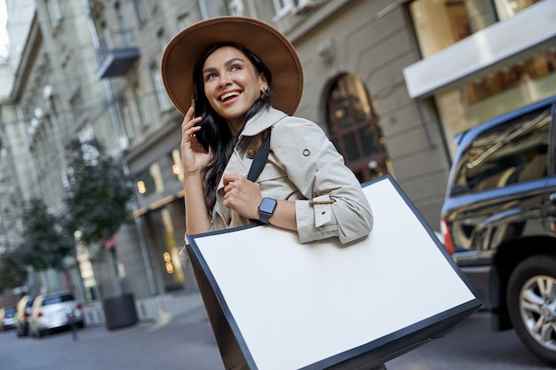 Ir de compras nos hace felices joven hermosa mujer emocionada con sombrero con bolsa de compras hablando sobre