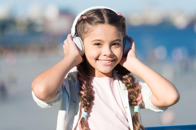 Ir con la corriente Adorable usuario de auriculares Niño pequeño con auriculares blancos ajustables Niña pequeña con auriculares inalámbricos bluetooth al aire libre Lindo niño escuchando música en auriculares estéreo