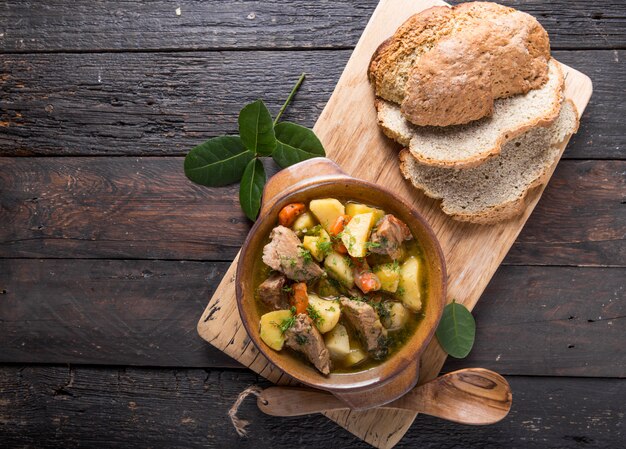 Irisches abendessen. rindfleisch mit kartoffeln, karotten und sodabrot gedünstet auf holztisch, draufsicht, kopierraum. hausgemachtes winterkomfortessen - langsam gekocht