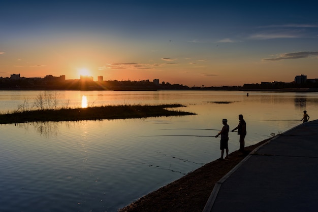 Irkutsk, Rusia - 13 de junio de 2020: silueta del hombre y el niño pescando en la orilla del río Angara en el sol del atardecer