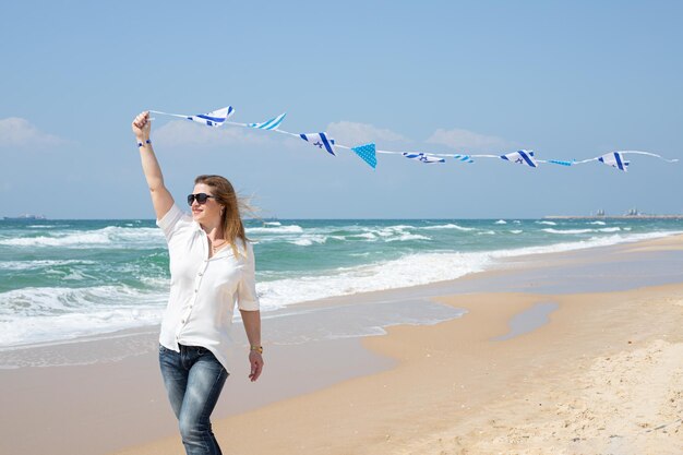 Irl feliz con una guirnalda de banderas de Israel en la orilla del mar Fiesta patriótica Día de la independencia Israel Yom Ha'atzmaut concepto