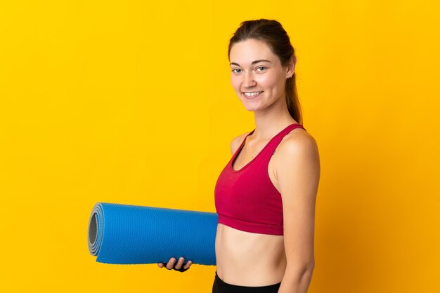 Irlanda joven mujer aislada sobre fondo amarillo con una estera y sonriendo