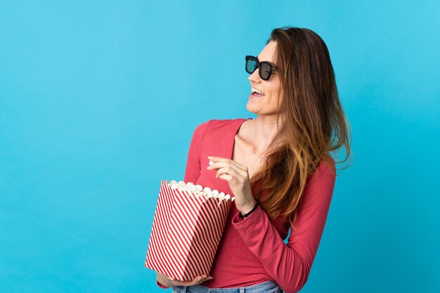 Irlanda joven mujer aislada sobre fondo azul con gafas 3d y sosteniendo un gran balde de palomitas de maíz