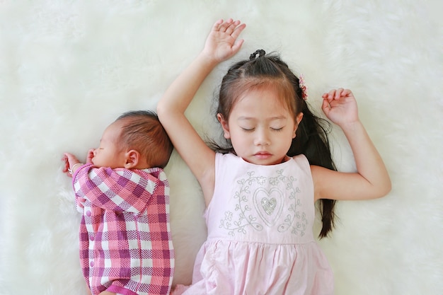 Irmã asiática e bebê recém-nascido que dormem junto no fundo branco da pele.