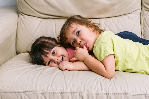 Irmã de duas meninas se abraçando, deitada em um sofá brincando