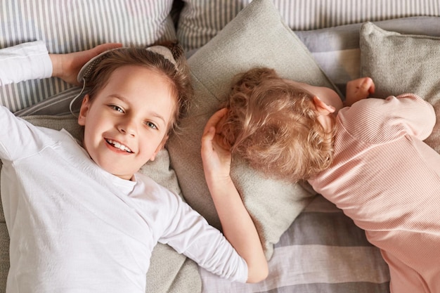 Irmã mais velha feliz com bebê dormindo deitado em uma cama juntos irmãos no quarto acordando expressando emoção positiva e felicidade