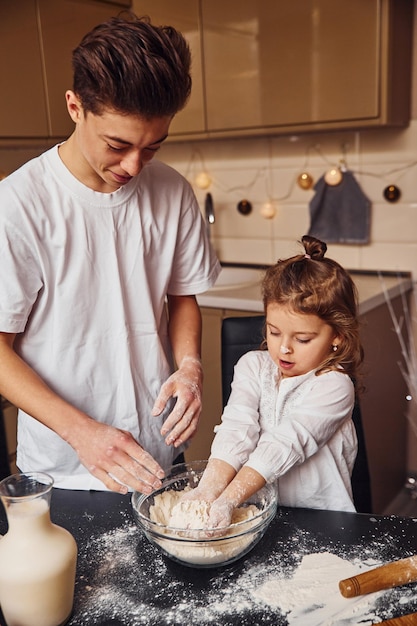 Irmão com sua irmã preparando comida usando farinha na cozinha e divirta-se.