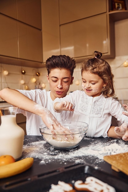 Irmão com sua irmã preparando comida usando farinha na cozinha e divirta-se.