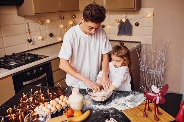 Irmão com sua irmã preparando comida usando farinha na cozinha e divirta-se.